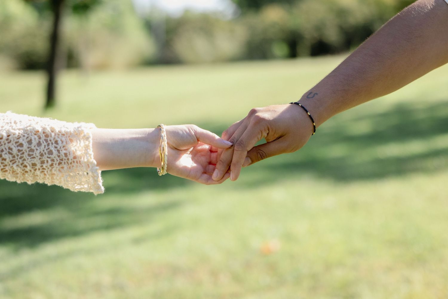 Adult and child holding hands outdoors in a sunny green park, symbolizing family bond and togetherness.