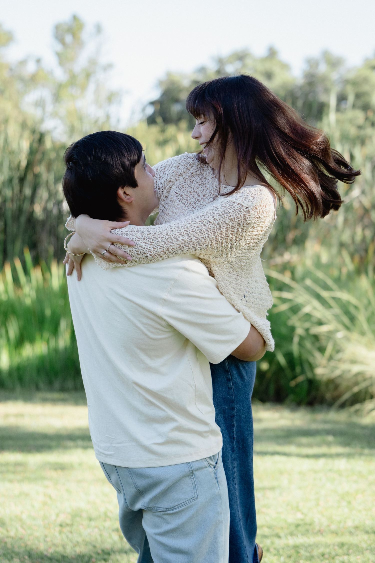 A couple embracing in a park, with the man lifting the woman as they share a joyful moment outdoors.