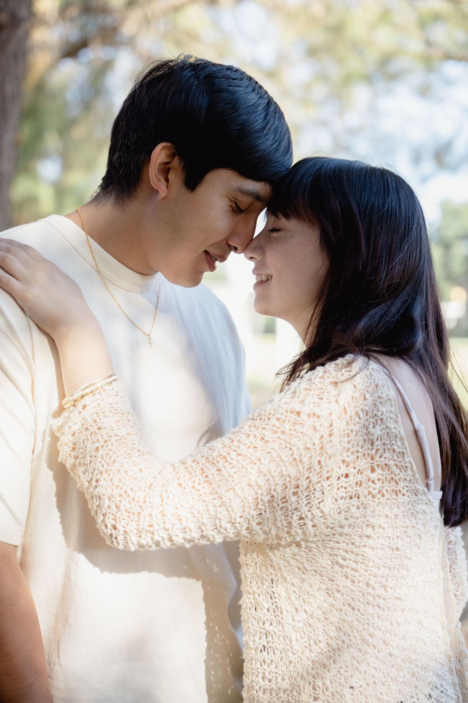 Young couple sharing a romantic moment outdoors, touching foreheads and smiling in soft natural light.