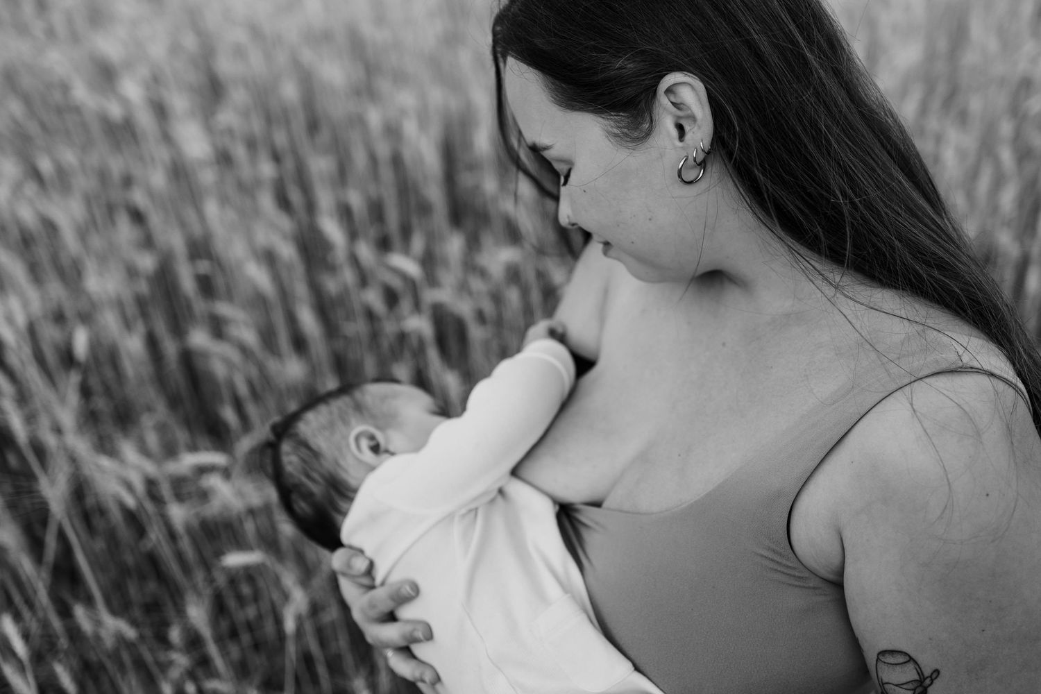 Black and white photo of a mother breastfeeding her newborn baby in a field of tall grass.