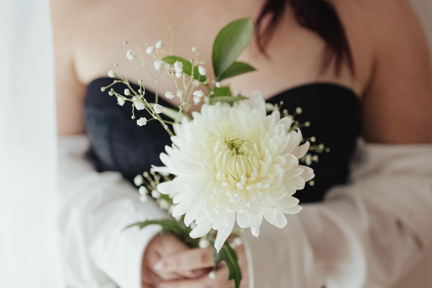 Woman in black strapless dress holding a white chrysanthemum bouquet with baby's breath and green leaves.