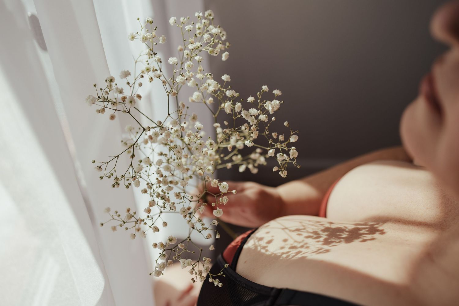Person holding delicate white baby's breath flowers near a sunlit window with soft shadows.