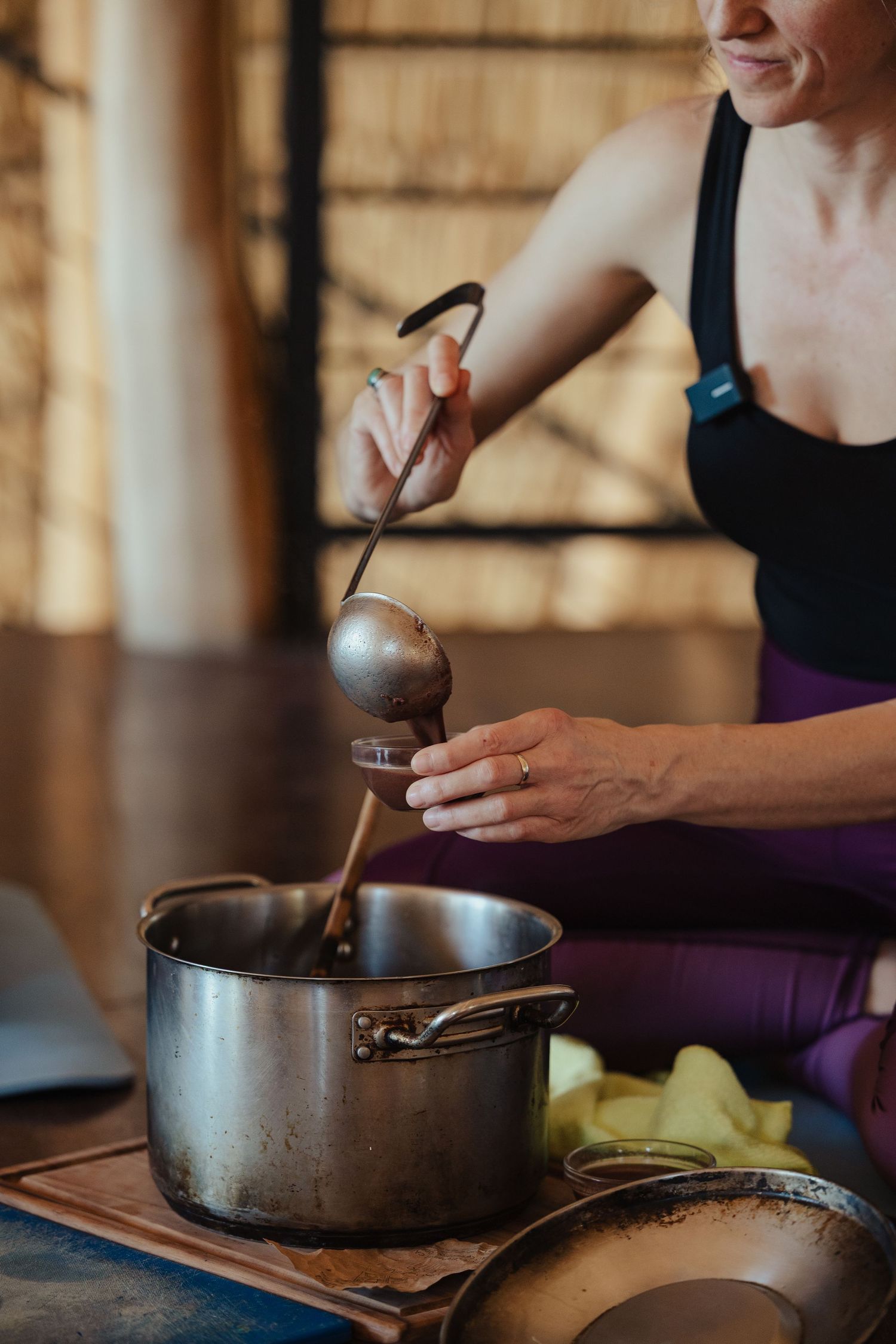Woman in activewear using a ladle to stir contents in a stainless steel pot while seated on the floor.