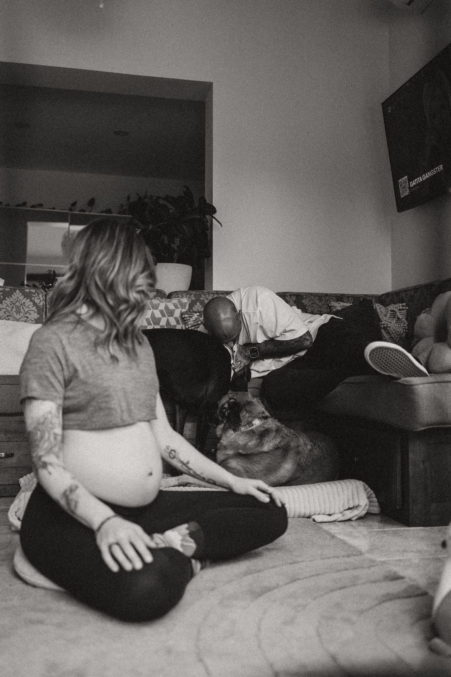 Pregnant woman sitting cross-legged on floor with dog in black and white photo.