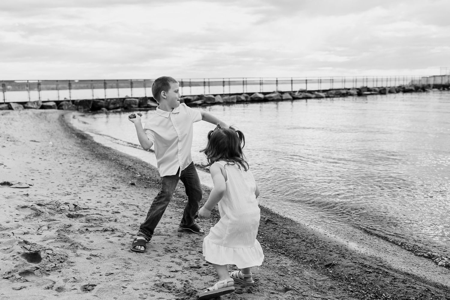 Two children playing on a sandy beach near the water in black and white photo.