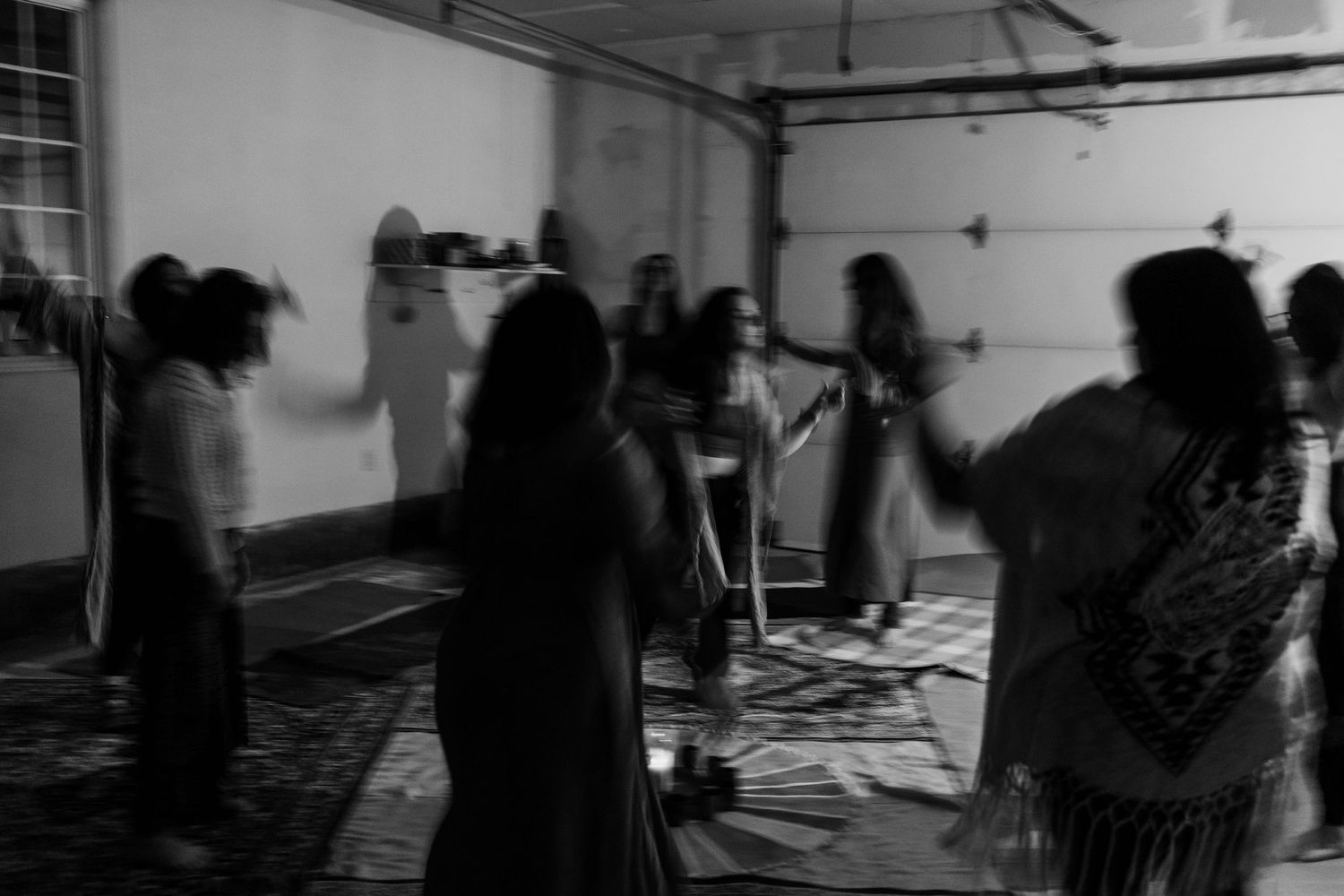 Black and white photo of women dancing together in a dimly lit room during a group gathering or ceremony.