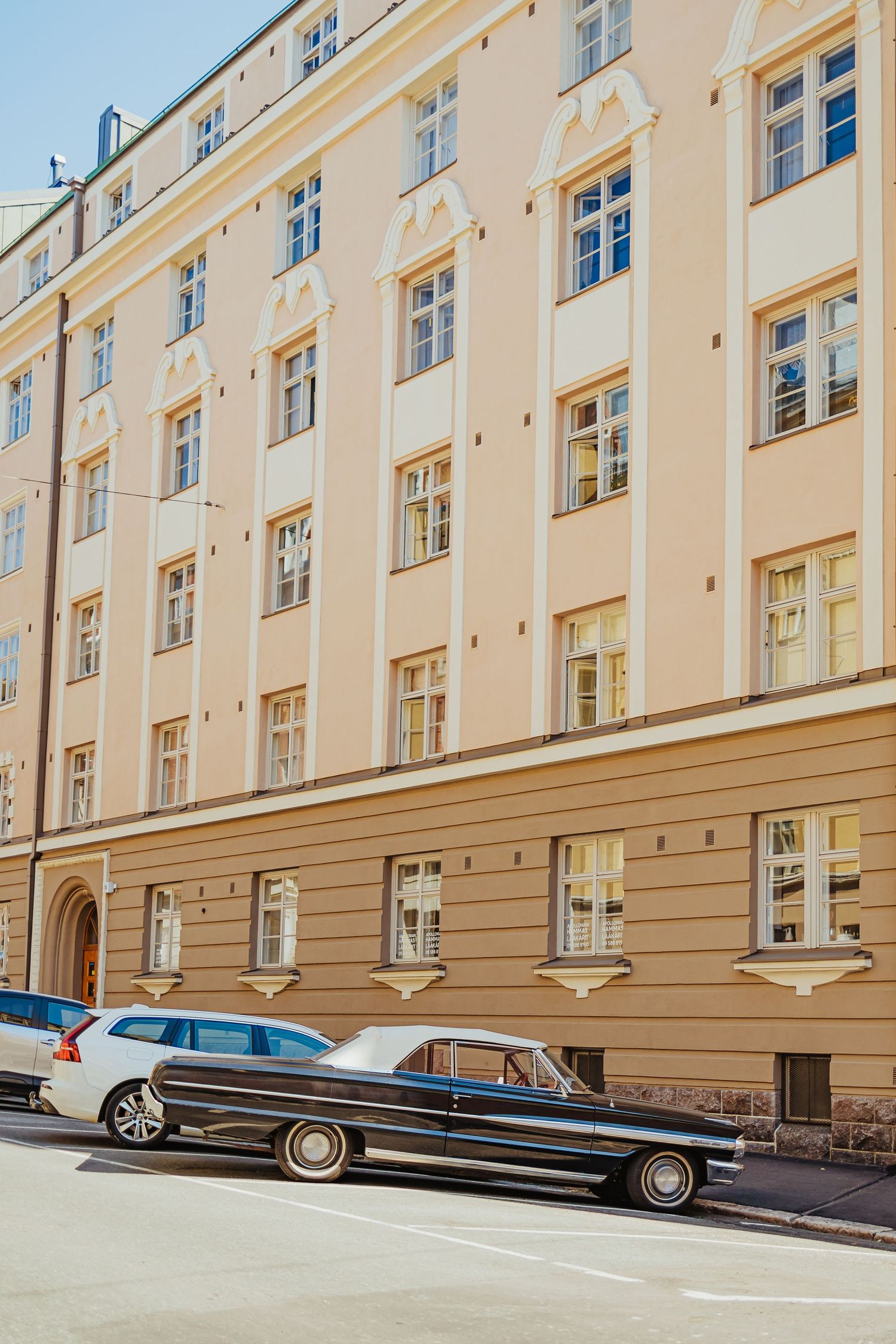 Vintage black car parked on a European street beside a classic cream-colored building with ornate architectural details.