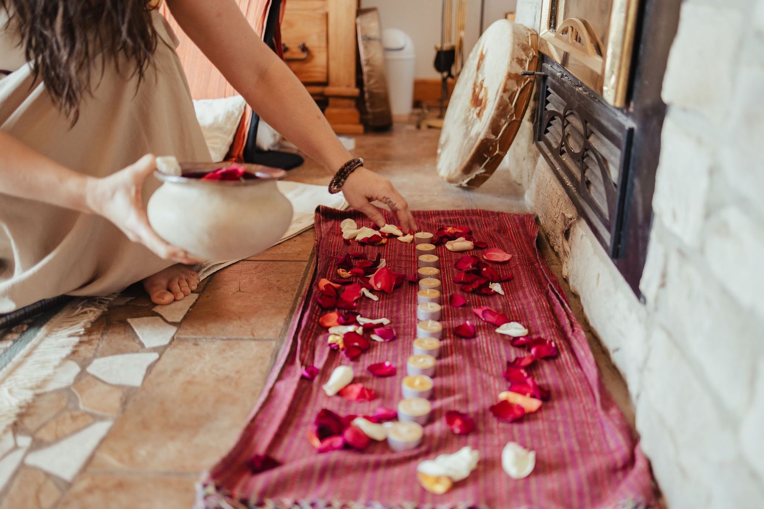 Person arranging red and white rose petals in a line on a decorative red mat.