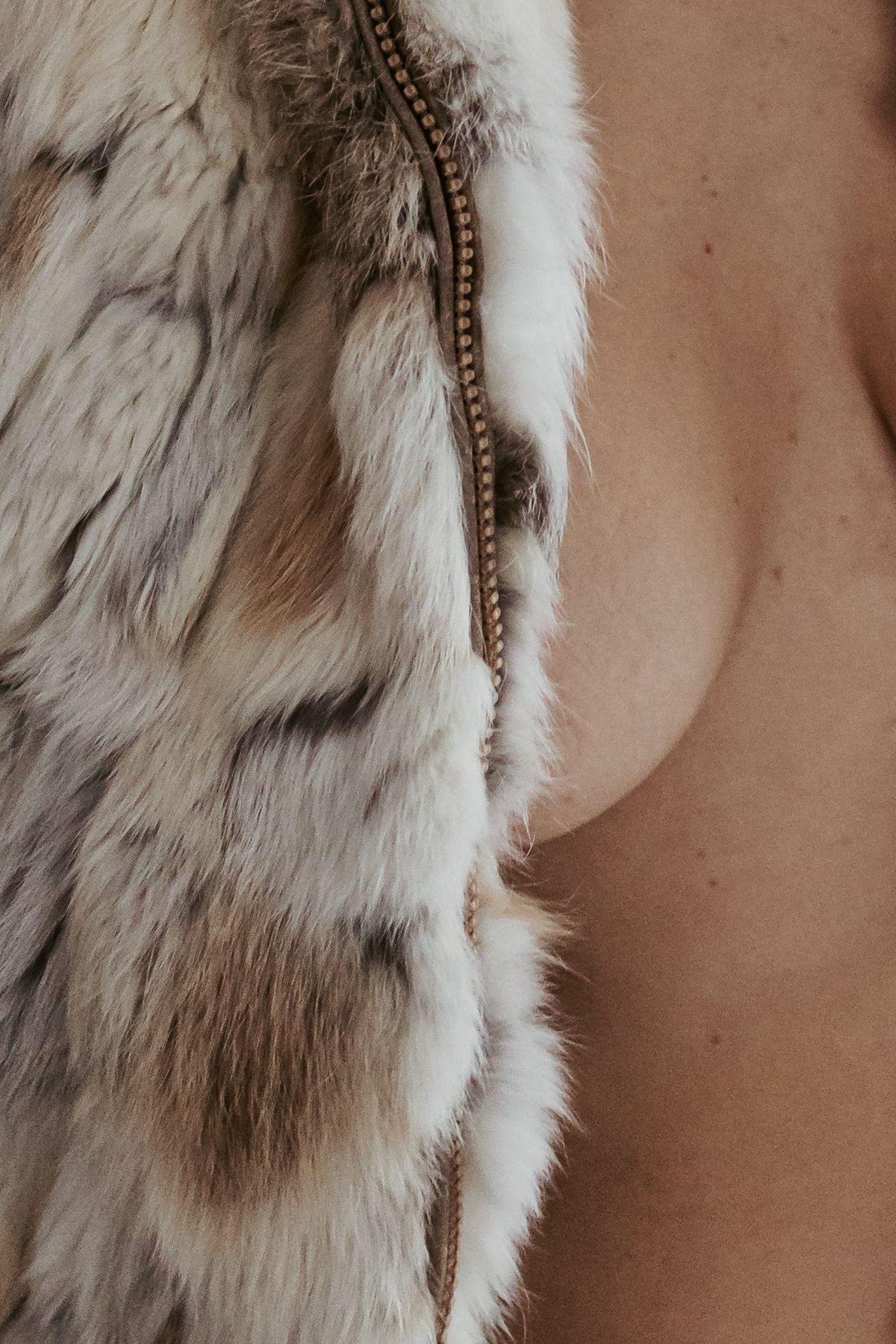Close-up of a luxurious white and brown spotted fur vest with a decorative zipper detail.