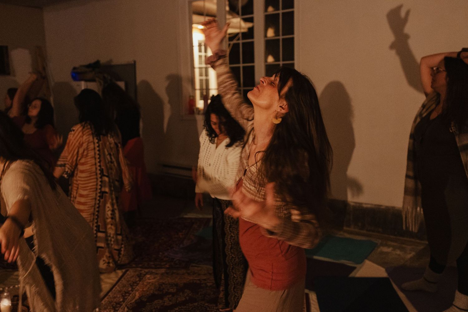 Woman dancing freely with arms raised in a dimly lit room during a group event.