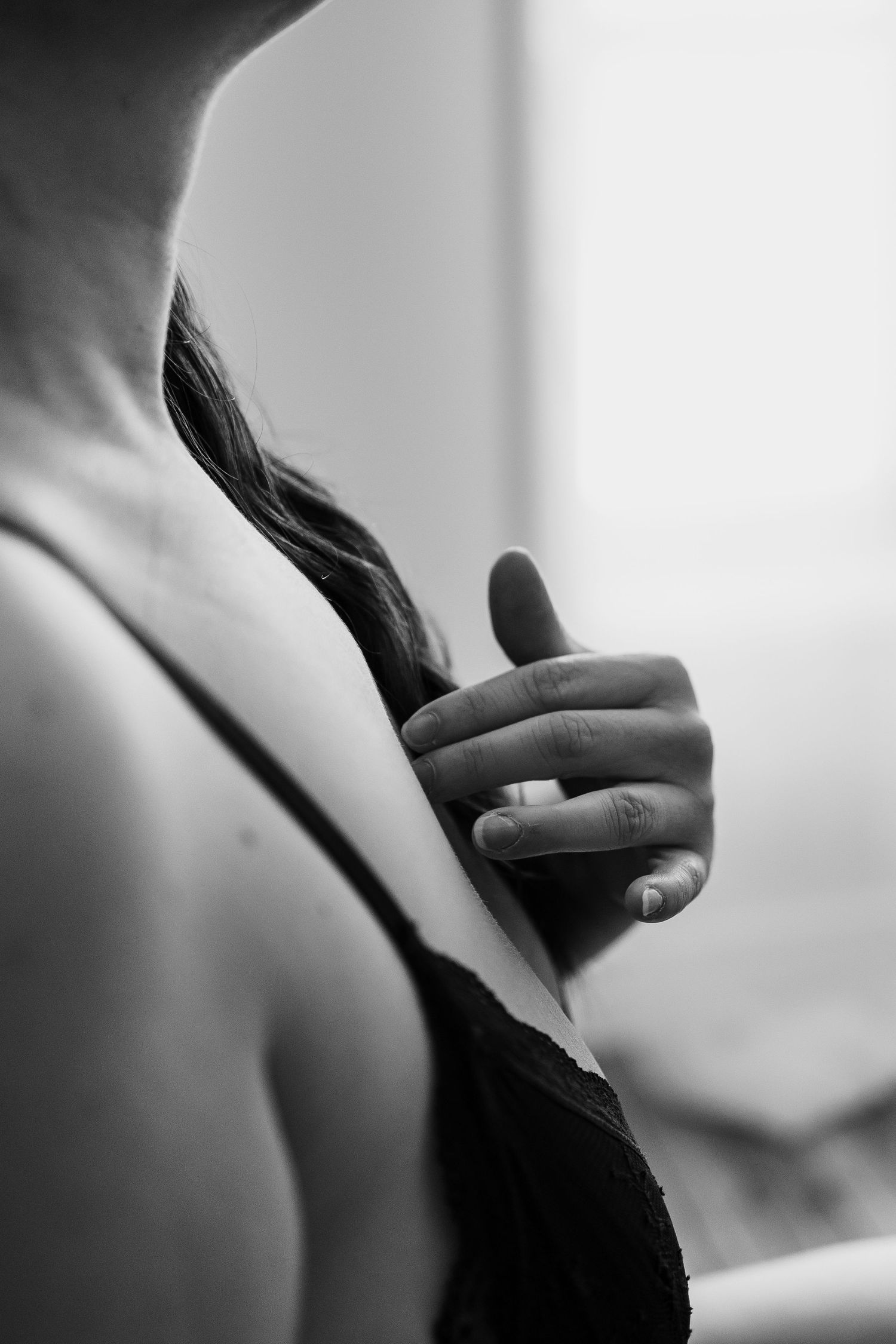 Black and white close-up of a woman holding her hair over her shoulder, wearing a dark lace bralette.