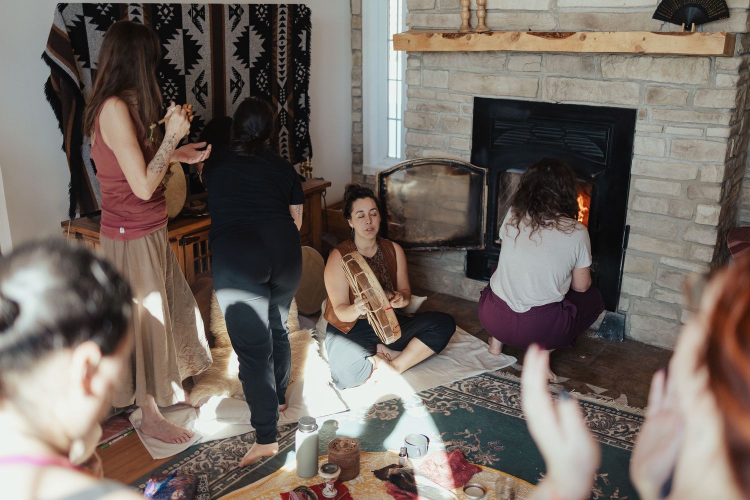 Women gathered around a fireplace in a cozy living room during an intimate spiritual or wellness gathering.