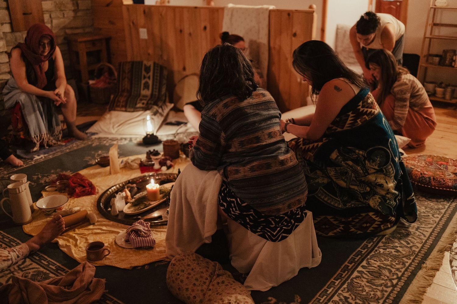 Women gathered around a candlelit altar on floor cushions in a cozy wooden room during a spiritual ceremony.