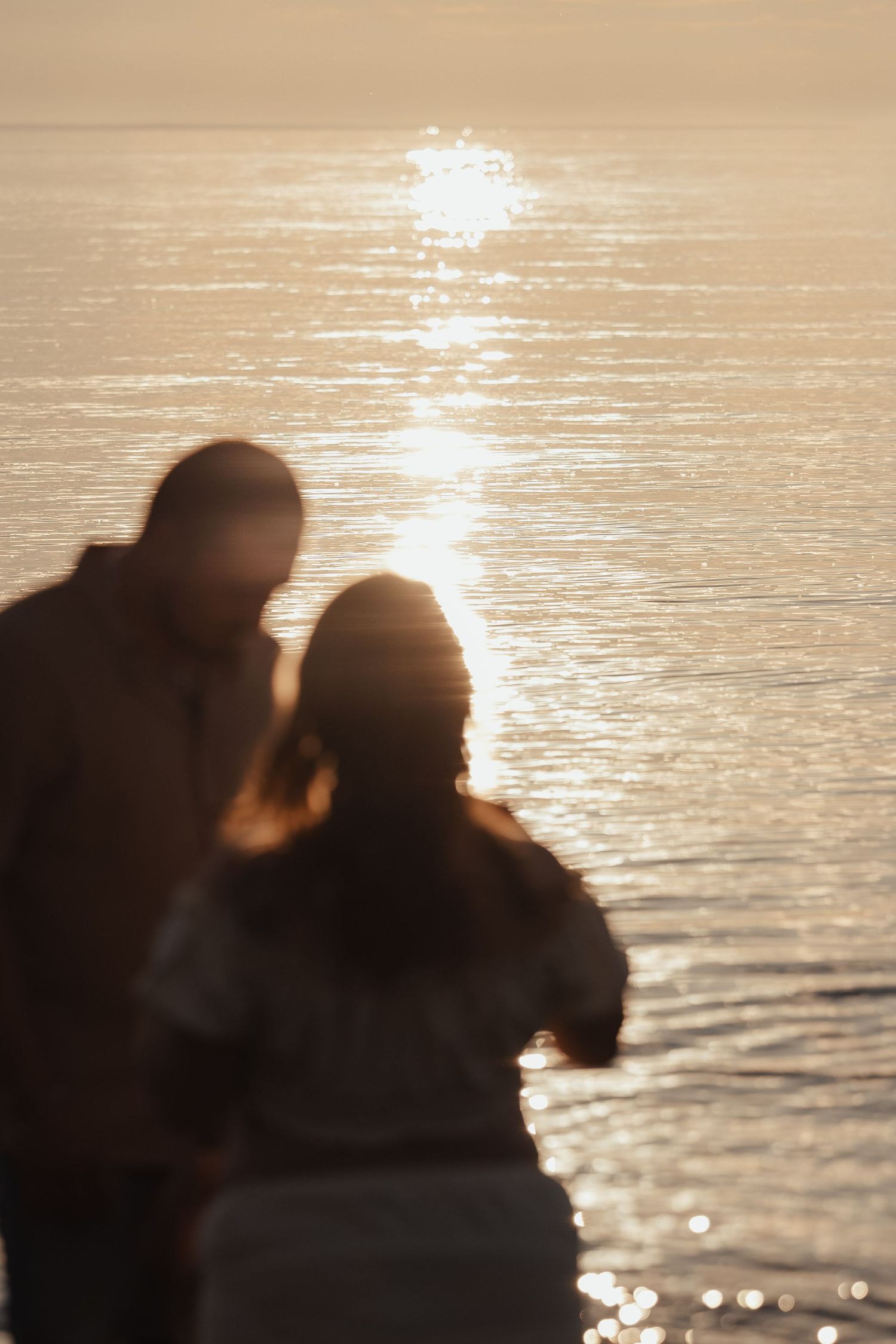 Blurred silhouette of a romantic couple standing together by the ocean at golden sunset.
