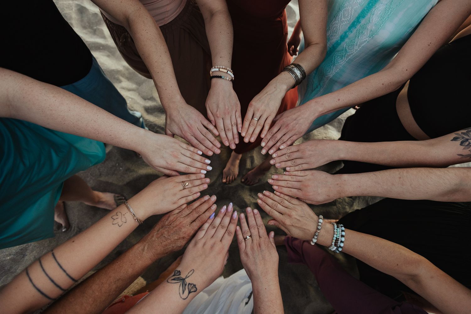 Group of women placing hands together in a circle, showing bracelets and tattoos in unity.