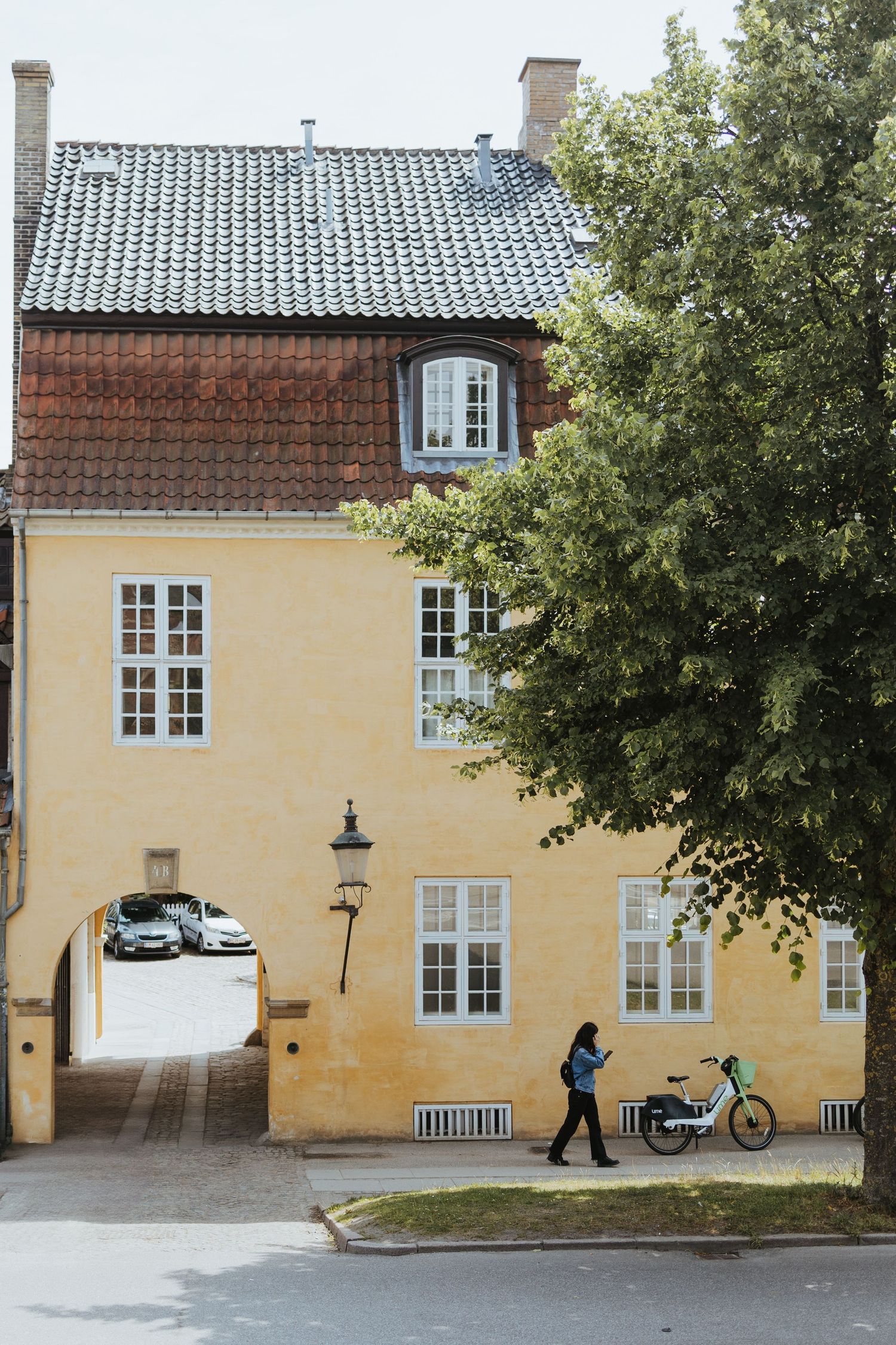 A person walks past a yellow historic building with white-framed windows and a bicycle parked outside in Copenhagen.