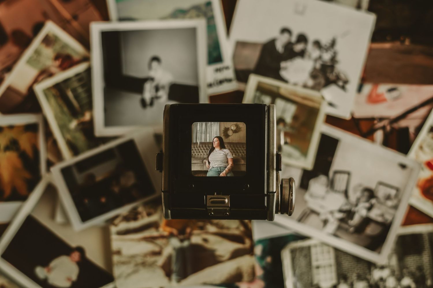 Vintage Polaroid camera surrounded by scattered black-and-white and color old photographs on a dark surface.