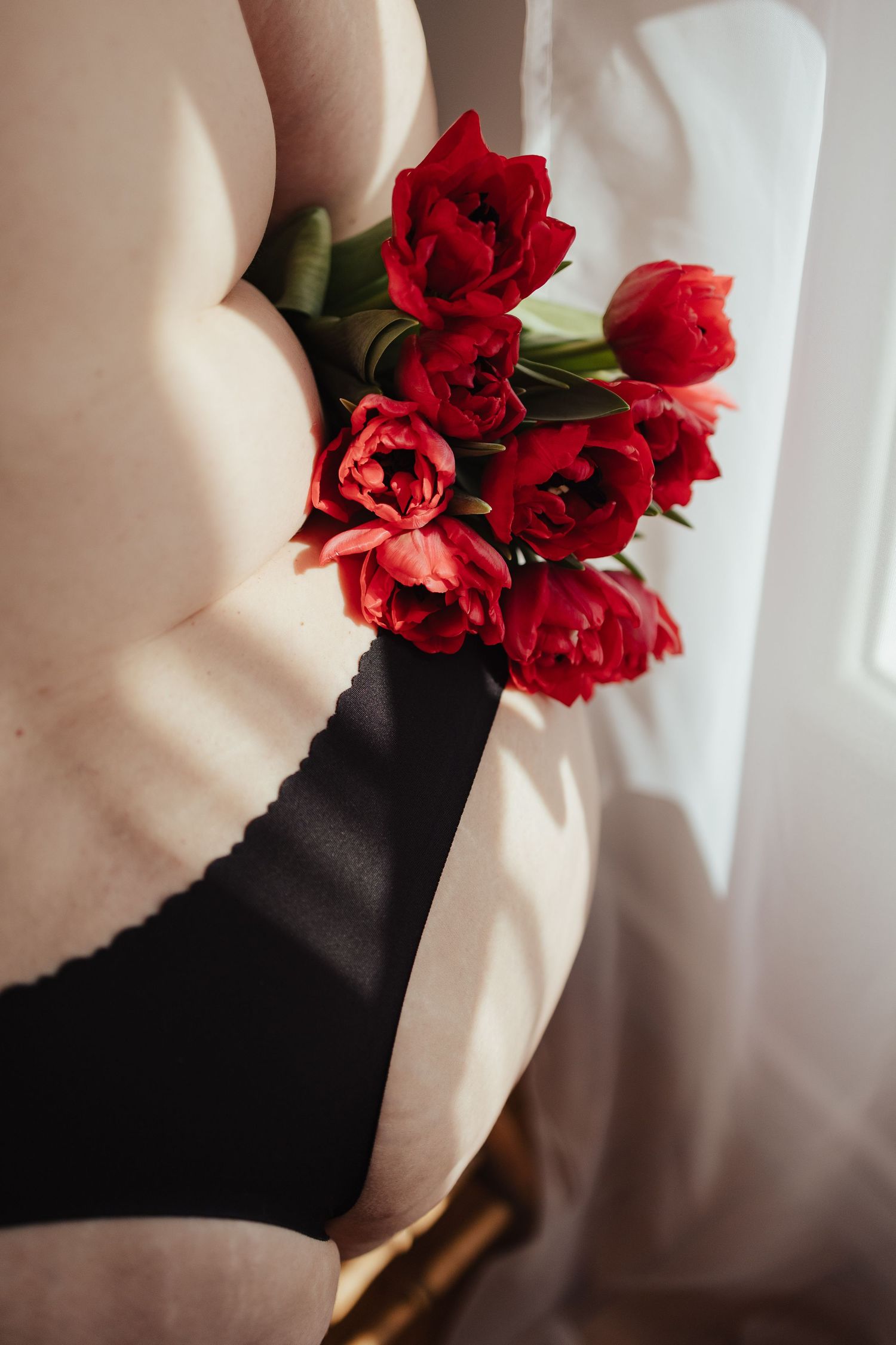 Person holding a bouquet of red tulips against a black lingerie top in soft natural light.