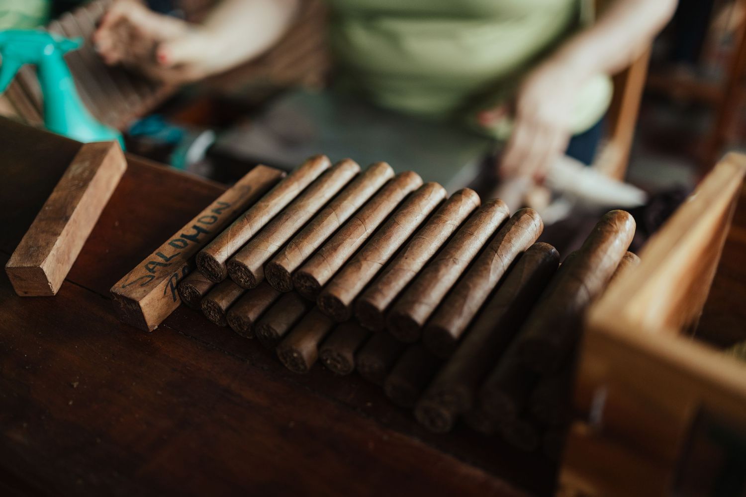 Handcrafted cigars lined up on a wooden workbench being rolled by a skilled artisan in a traditional cigar factory.