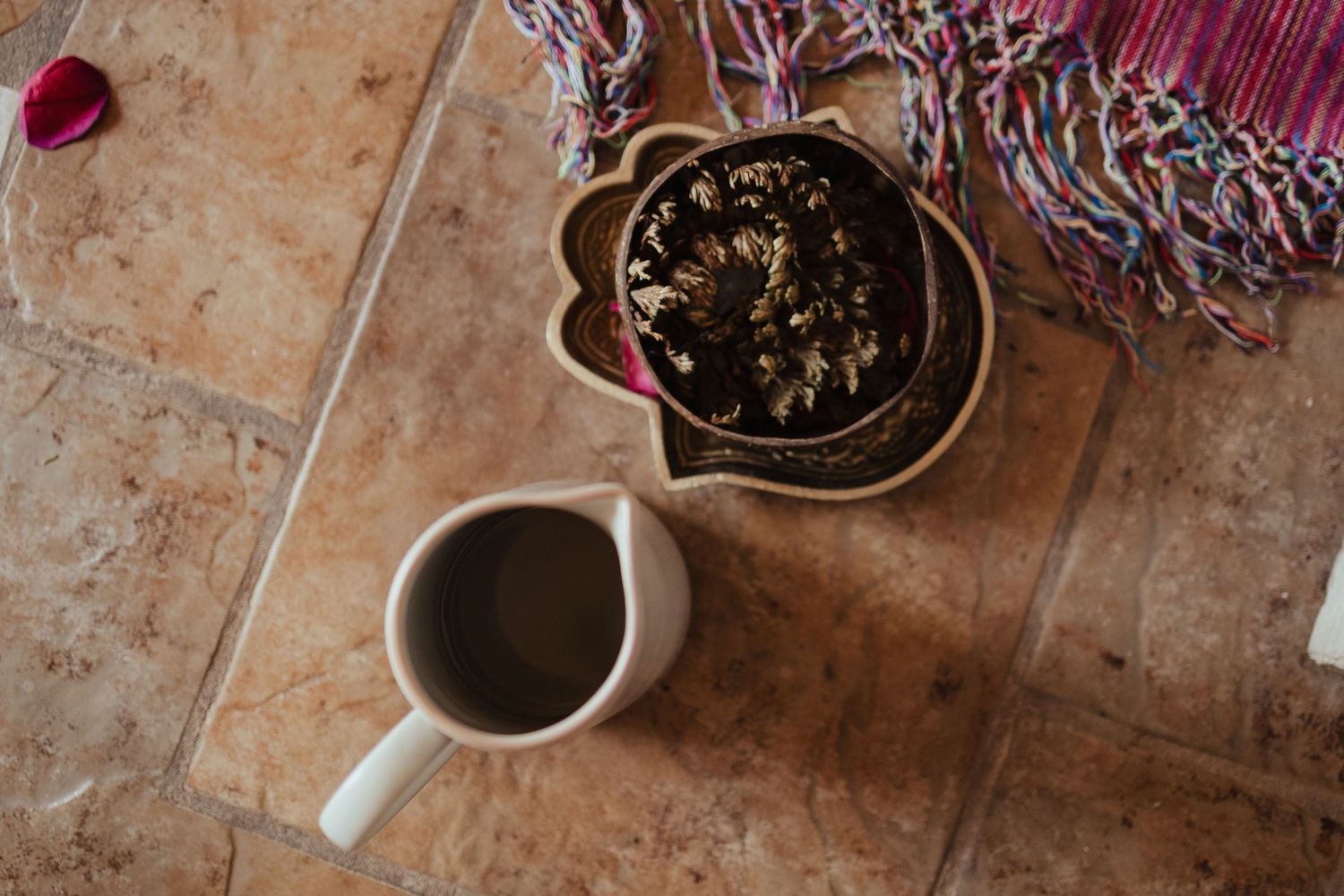 Overhead view of a coffee mug and cactus plant in decorative pot on terracotta tile floor with colorful textile.