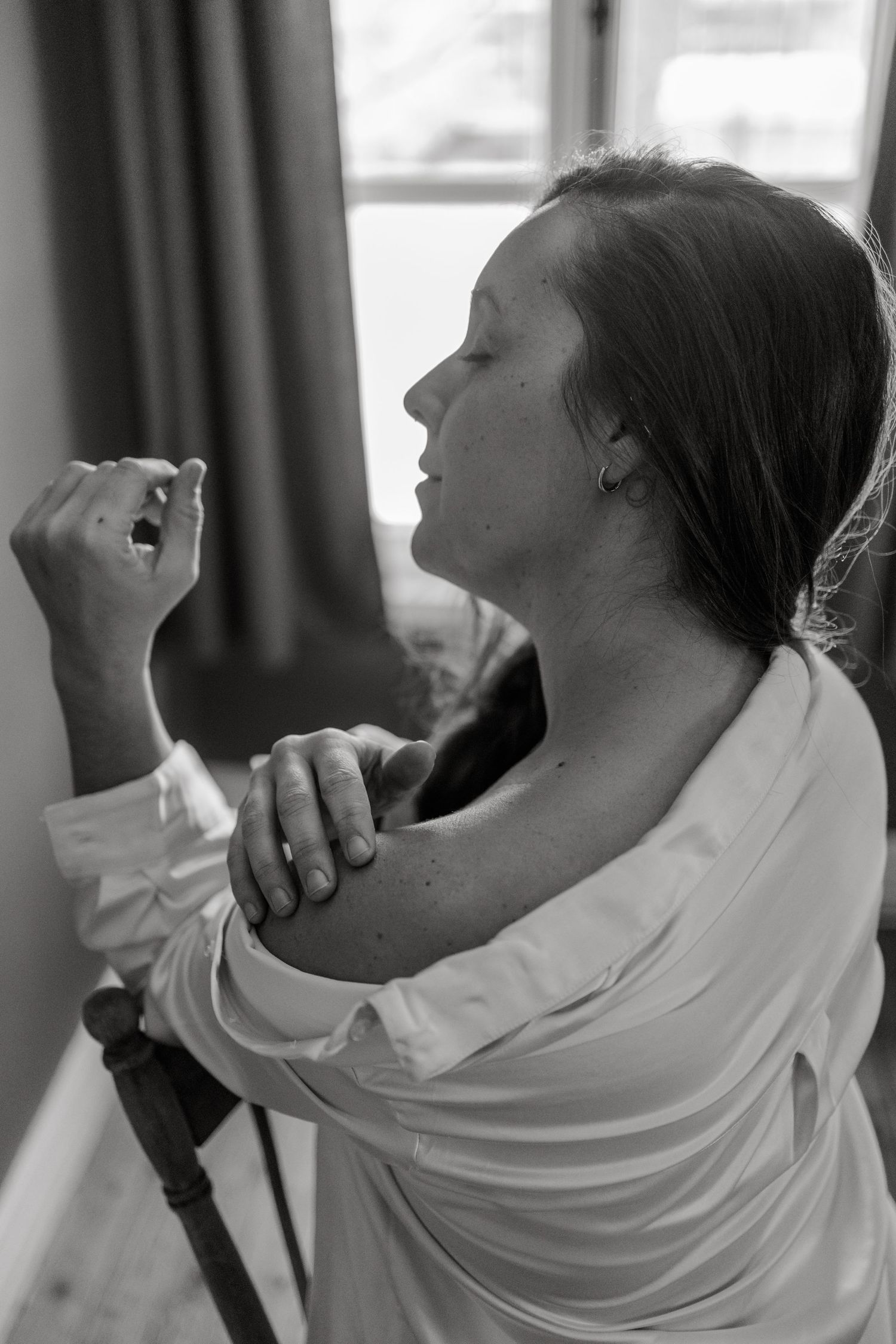 Black and white photo of a woman in white shirt holding a small object near her face indoors.