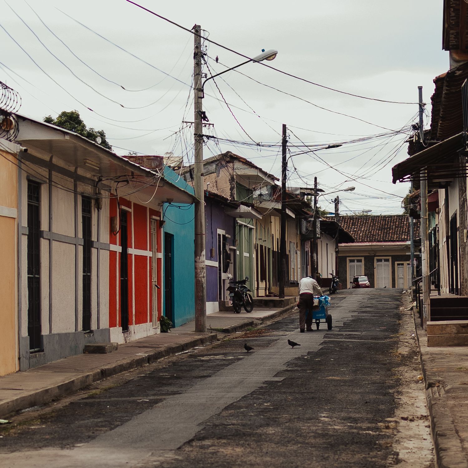 Colorful colonial street in a Latin American town with power lines overhead and a person pushing a stroller.