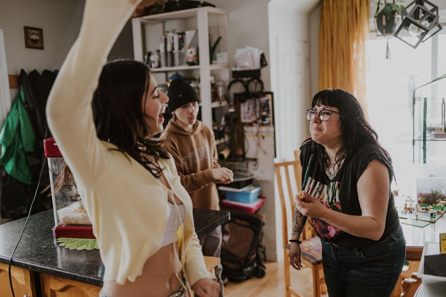 Three women socializing indoors, one with raised arm, in a cozy home setting with natural light.