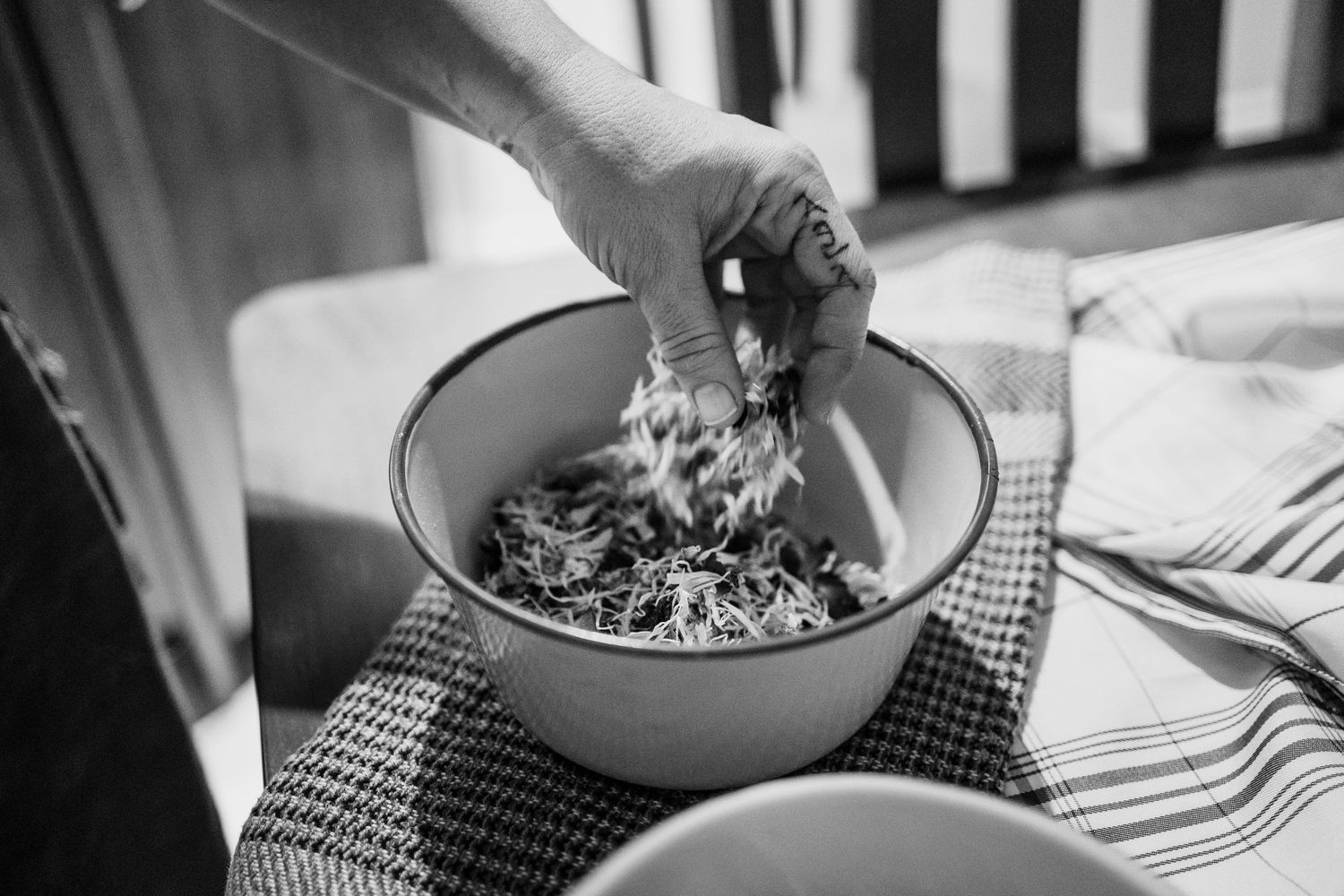 Hand mixing fresh ingredients in a white bowl on a checkered cloth, black and white photo.
