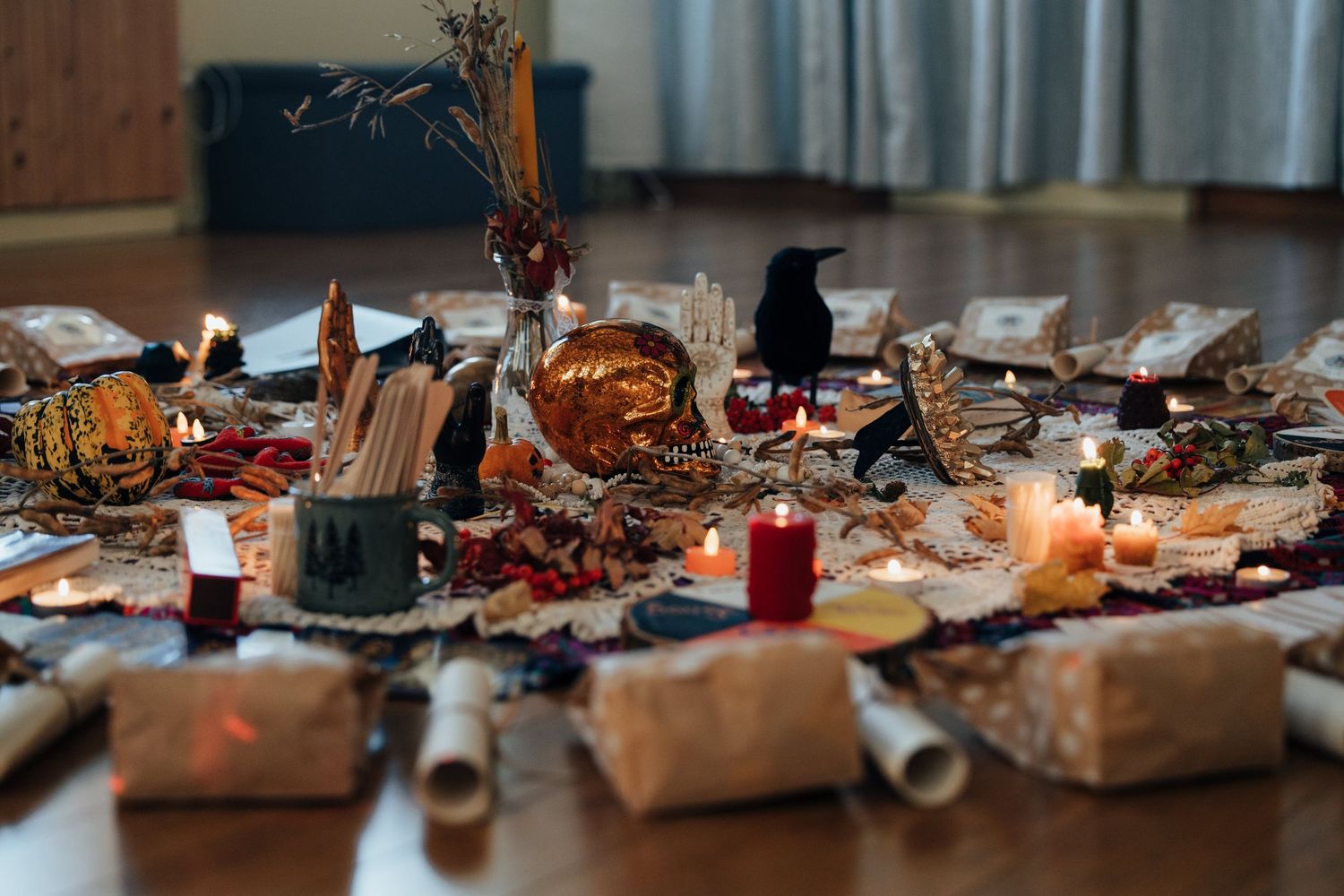Mystical altar display with candles, crystals, pumpkins, and autumn botanicals arranged on a wooden floor.