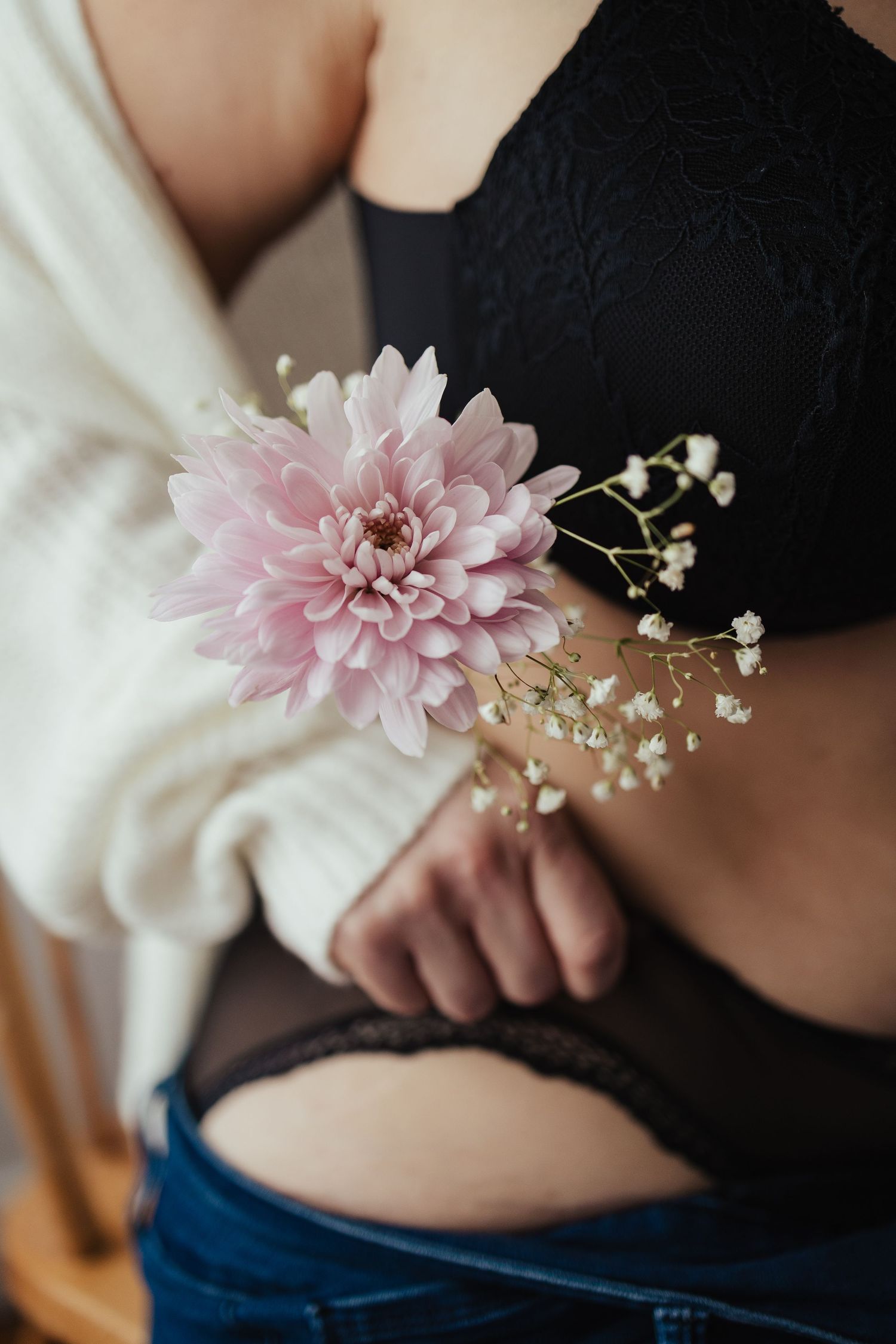 Woman in black lace bralette and jeans holding a pink dahlia with baby's breath flowers.
