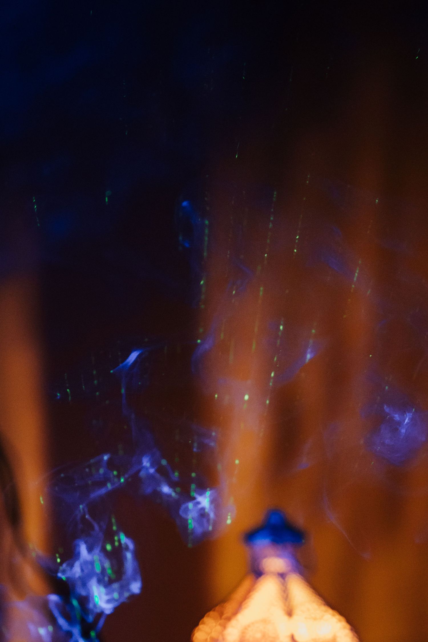 Mystical blue smoke and light particles swirling against a dark orange background with a glowing object below.