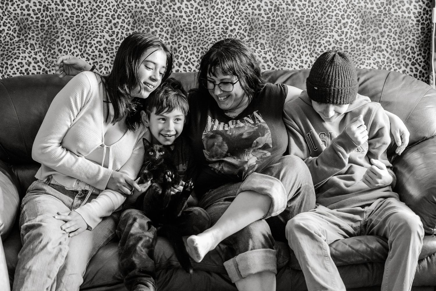 Black and white photo of four people sitting together on a couch, smiling and sharing a joyful moment.