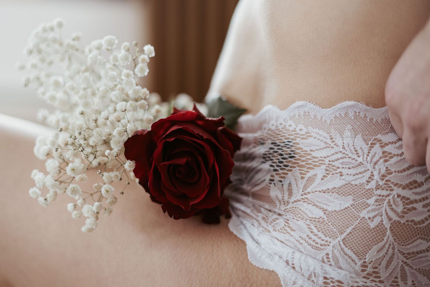 Close-up of a red rose and baby's breath tucked into white lace lingerie against soft skin.