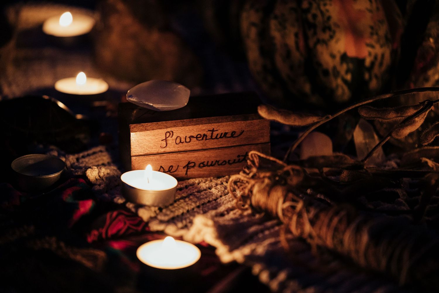 Candlelit wooden box inscribed with French text surrounded by glowing tea light candles on a decorative cloth.