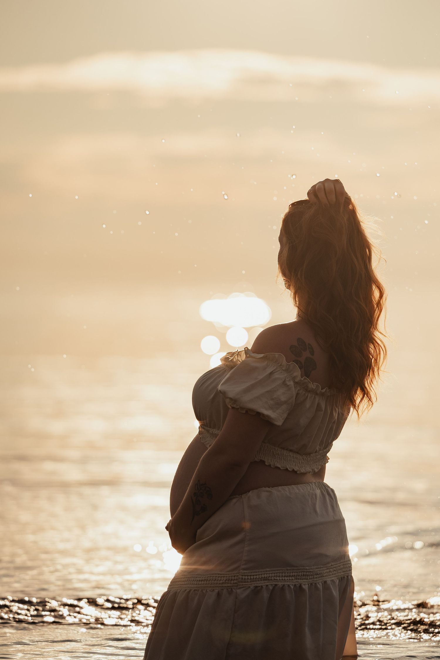 Silhouette of pregnant woman cradling belly at golden sunset by the sea.