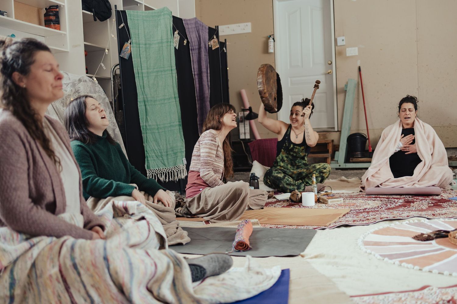 Women sitting in a circle on floor mats during a group meditation or wellness retreat session indoors.