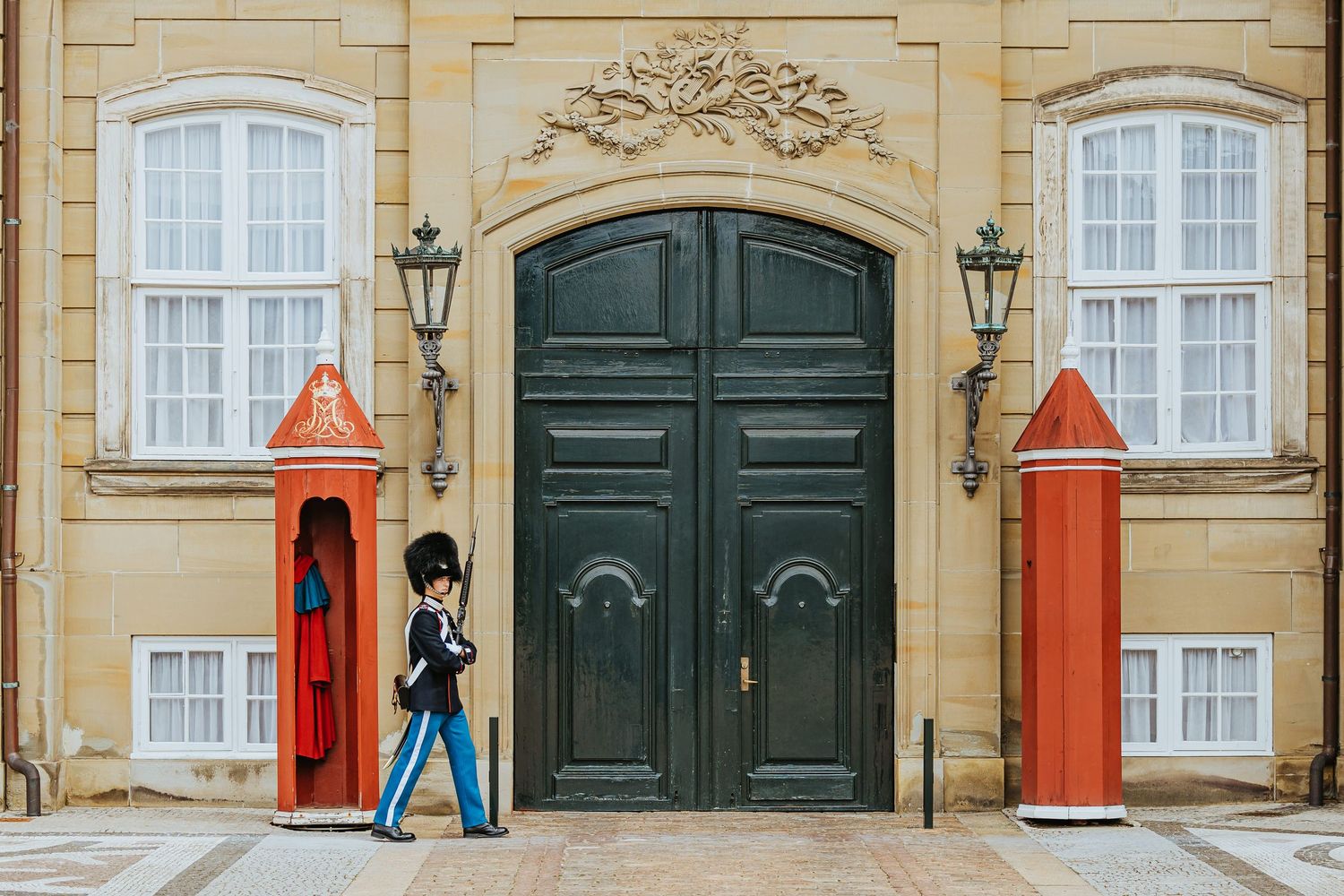 Royal Guard marching in front of ornate palace doors at Amalienborg Palace, Copenhagen, Denmark.