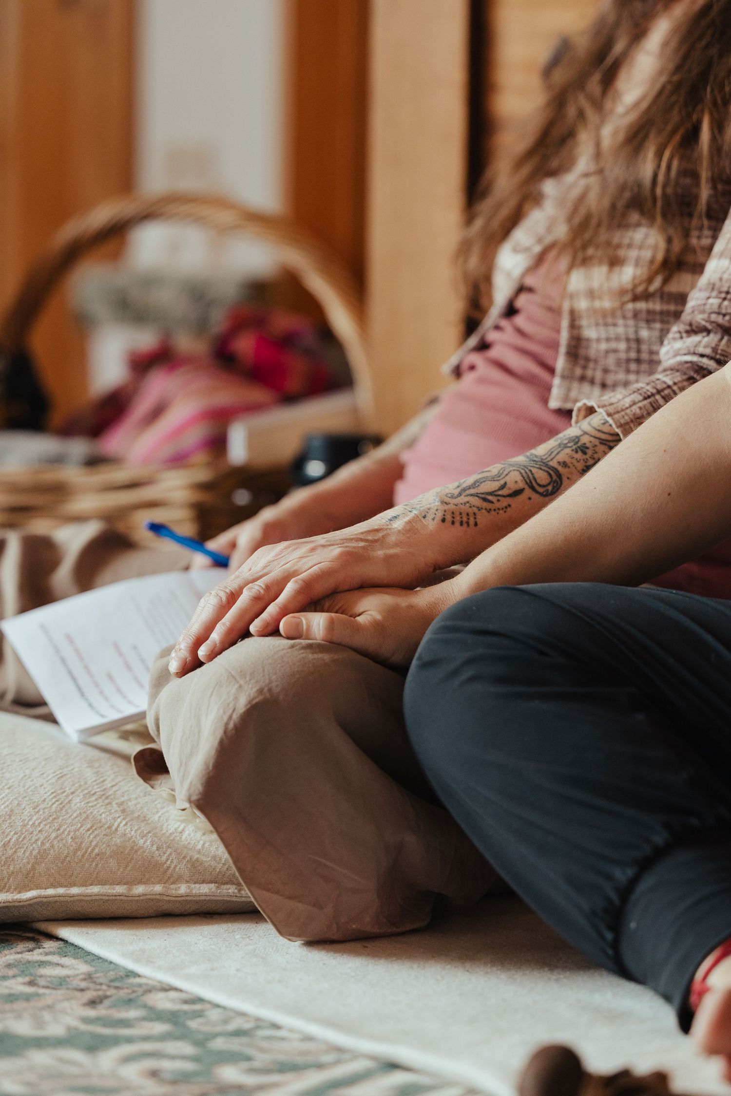 Woman with tattoed arm sitting cross-legged on floor with papers nearby in cozy home setting.