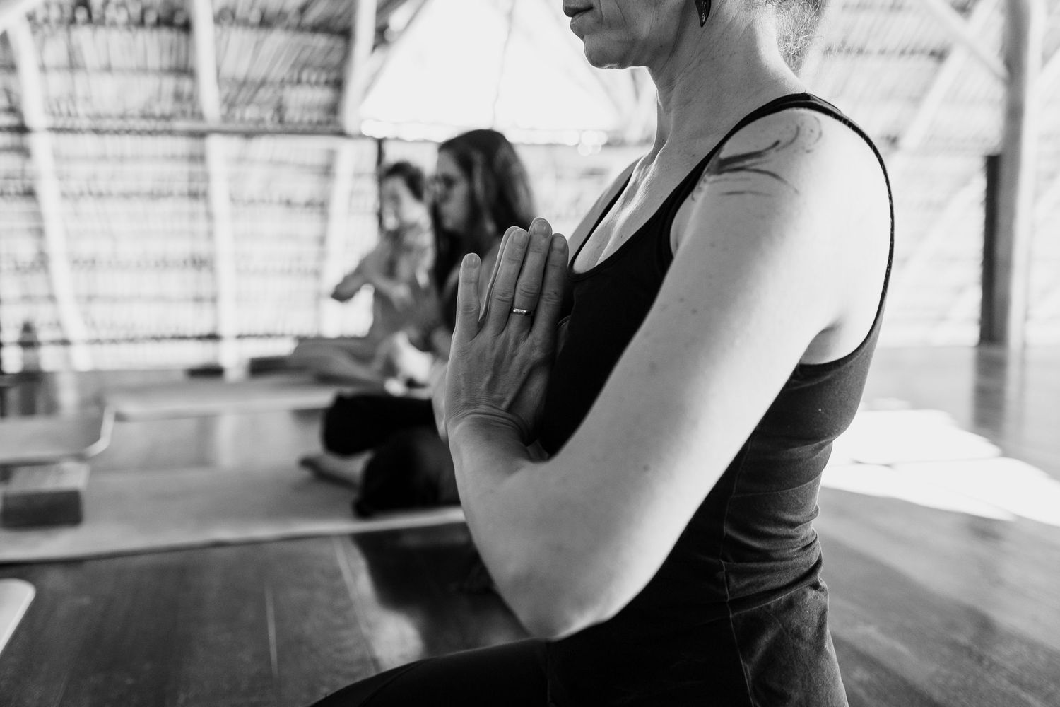 Black and white photo of women practicing yoga in namaste pose inside an open-air studio.