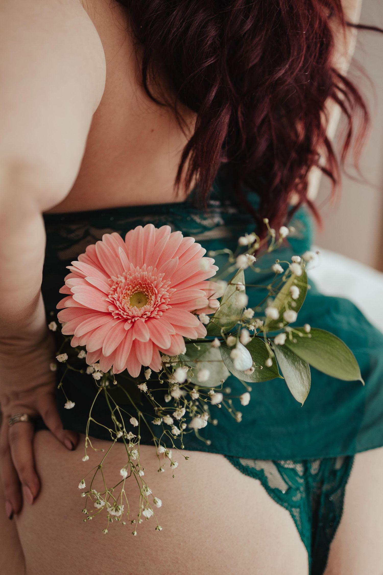 Woman in teal lace lingerie holding a pink gerbera daisy with baby's breath flowers against her back.