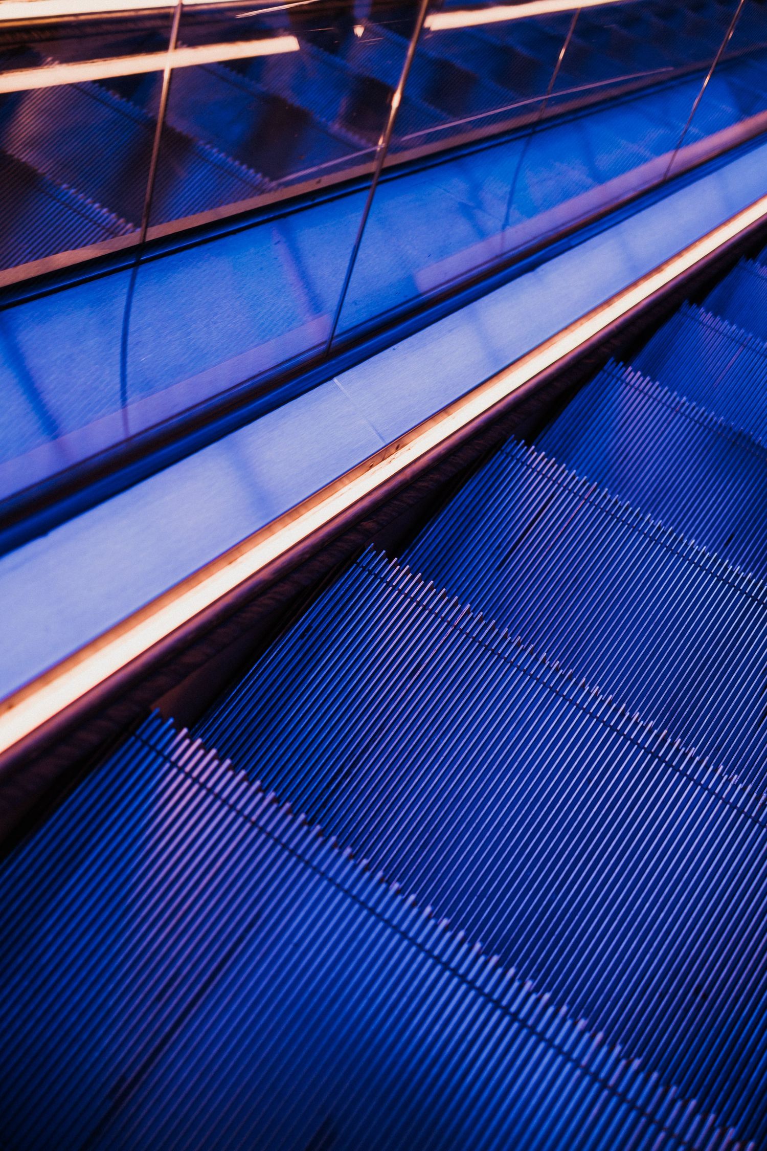 Blue-lit escalator with glowing handrails and ribbed metal steps in a modern building.