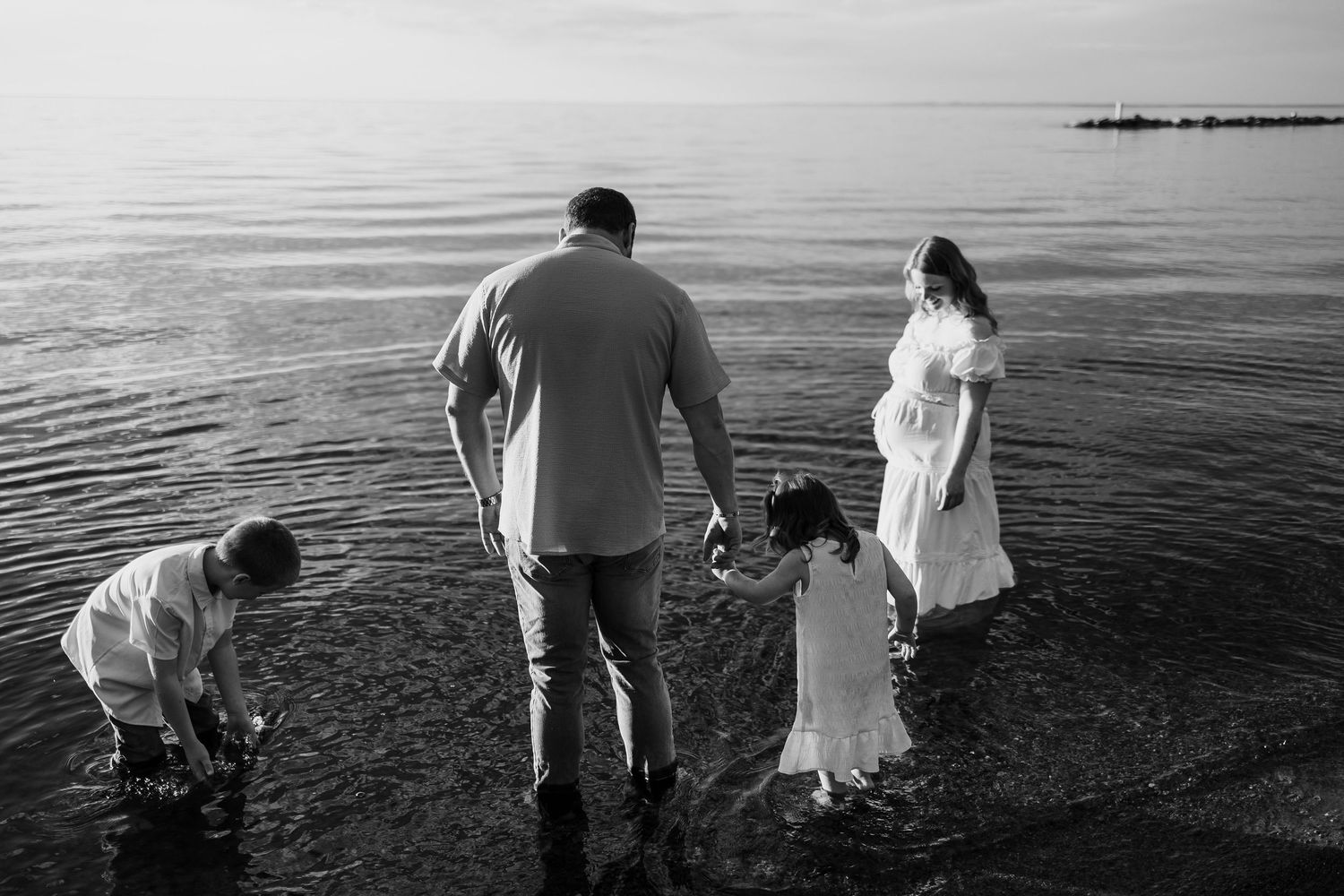 Black and white family photo of parents and two children wading in calm ocean water.