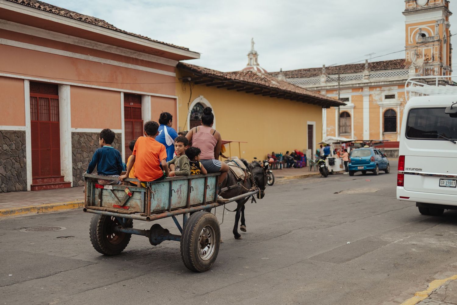 Children riding a horse-drawn cart through colorful colonial streets in Granada, Nicaragua.