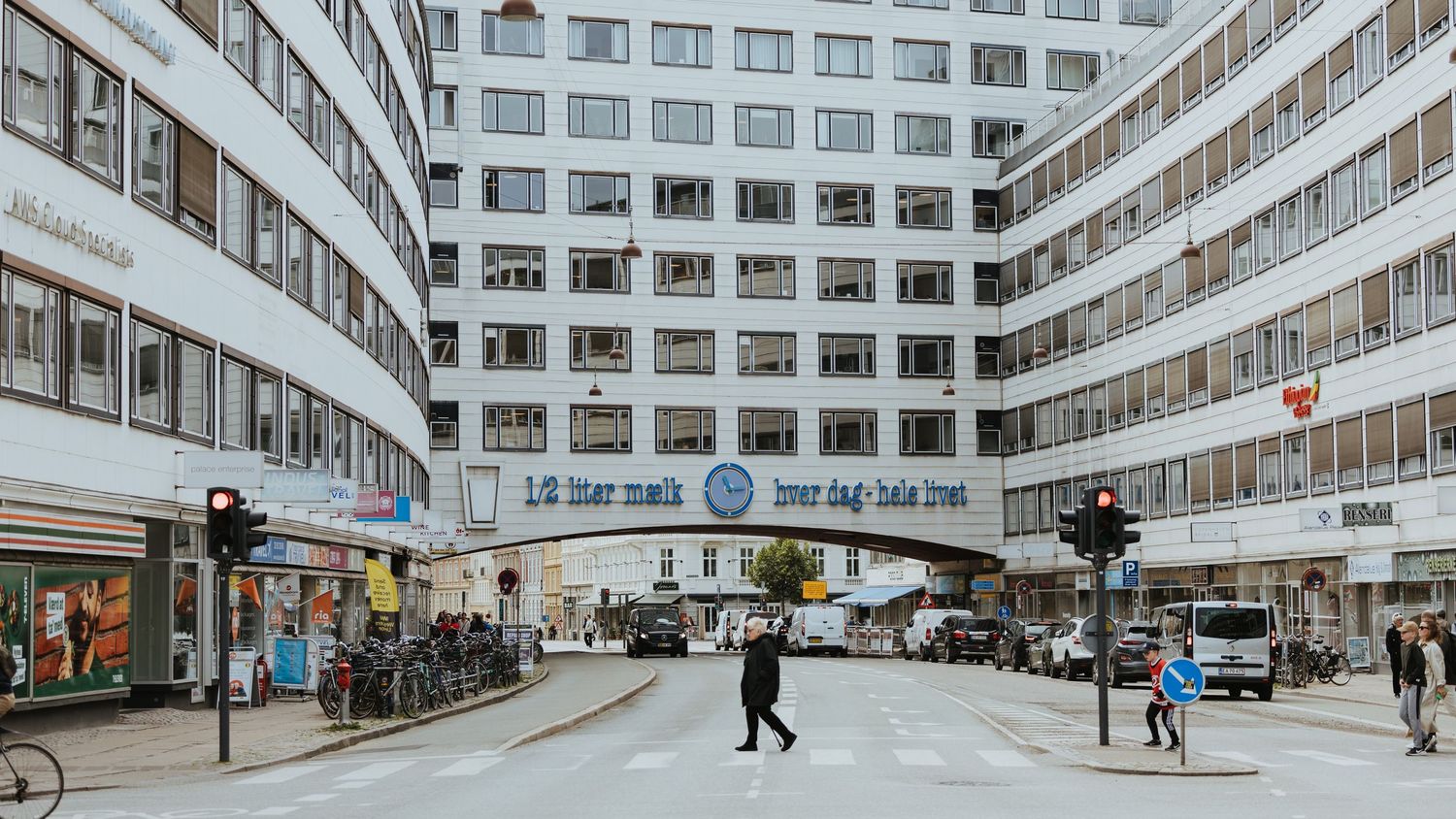Curved modernist building facade with pedestrians crossing street in urban city square.