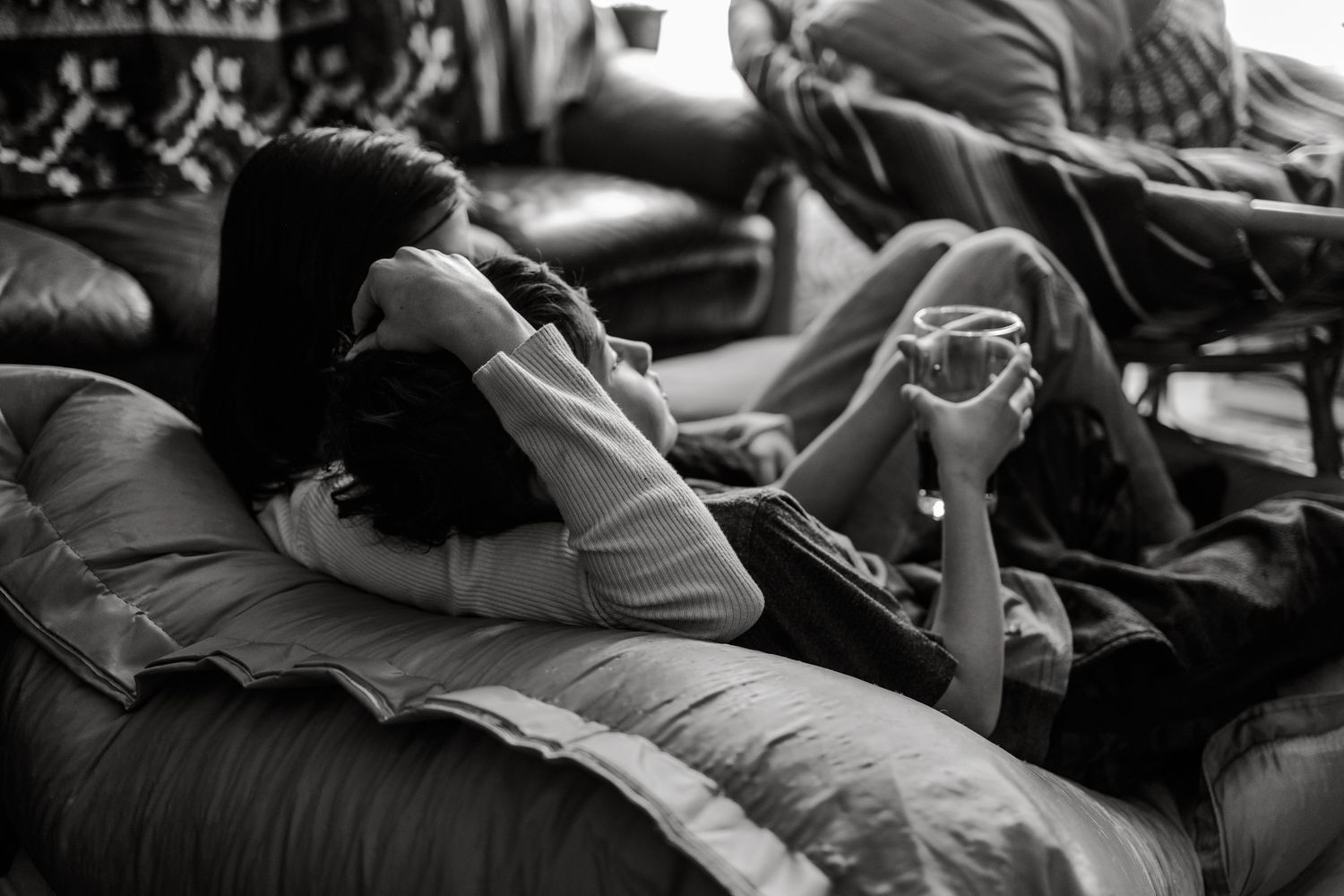 Black and white photo of two people relaxing on leather bean bag chairs, one talking on phone.
