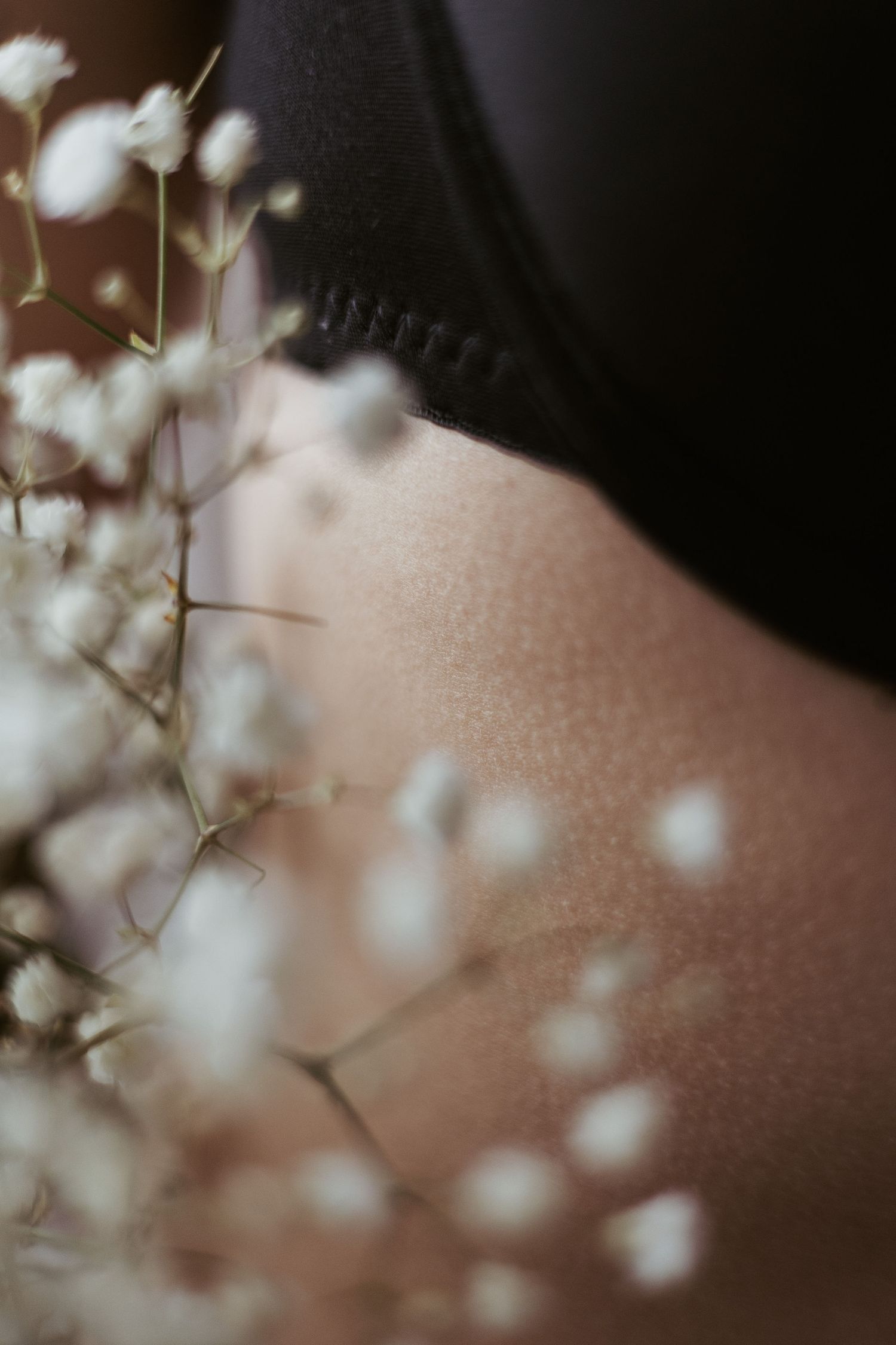 Close-up of baby's breath flowers against bare skin and black fabric in soft focus.