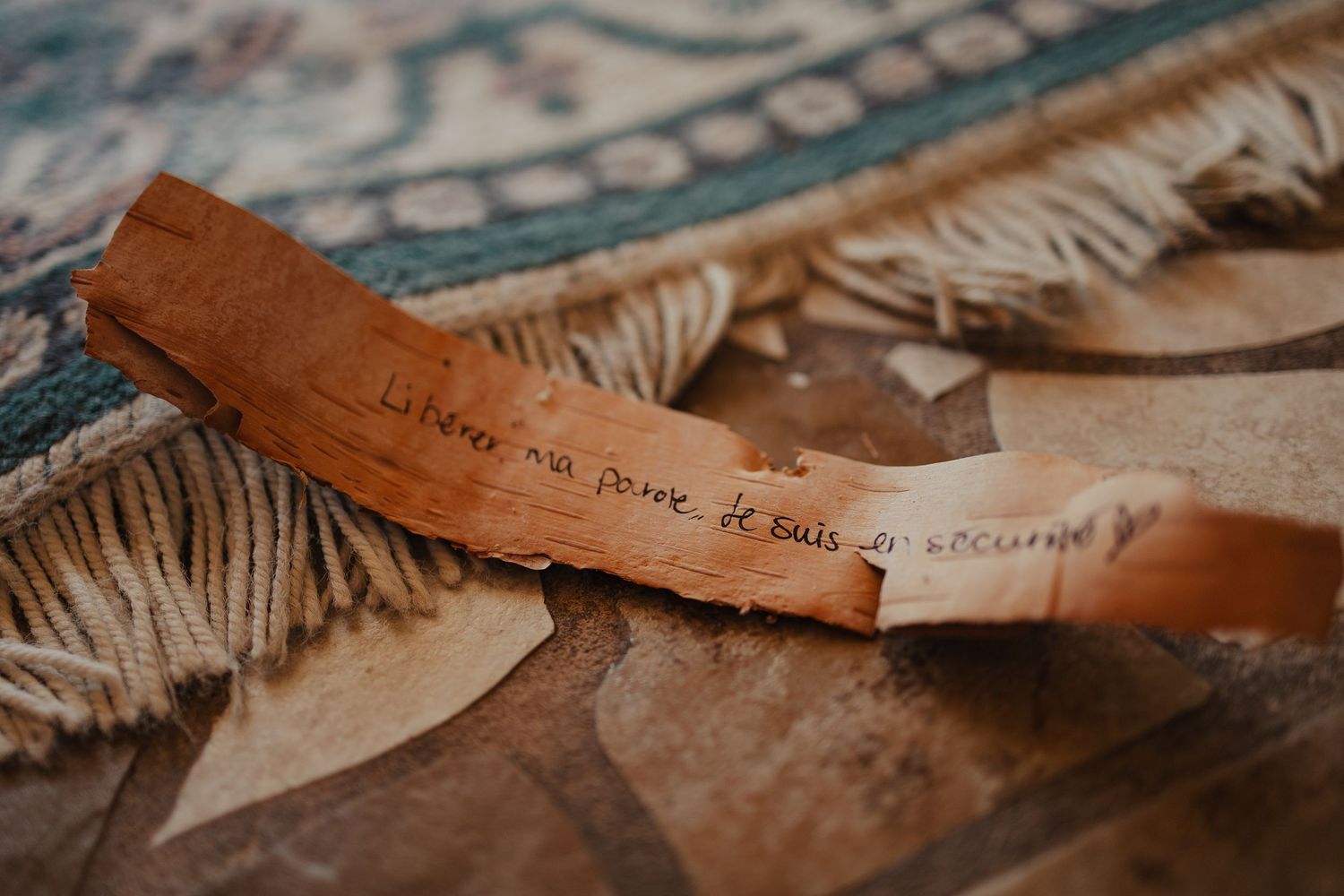 A curled piece of brown leather with handwritten French text resting on a decorative rug.