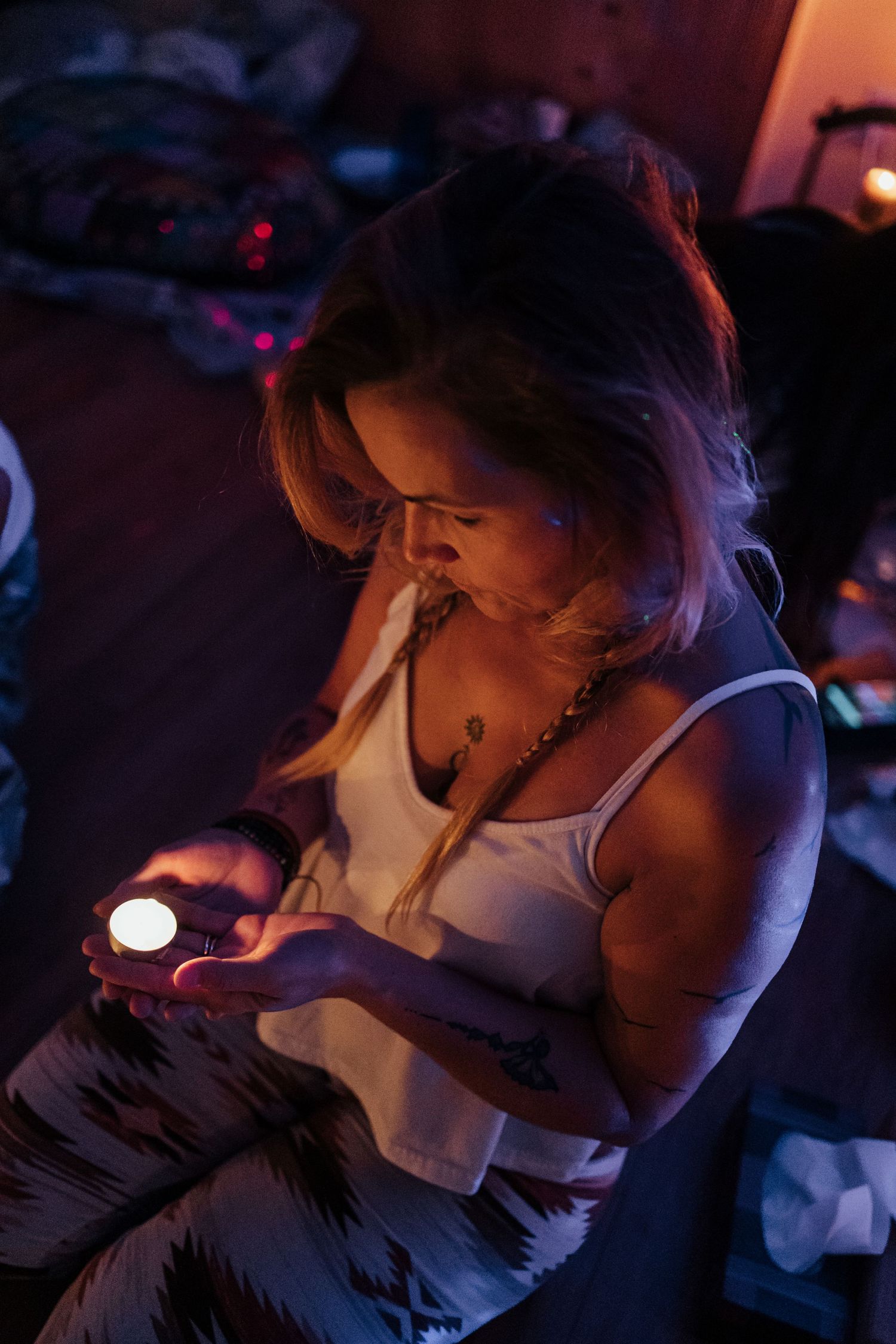 Woman holding a glowing candle in a dimly lit room with purple and orange ambient lighting.