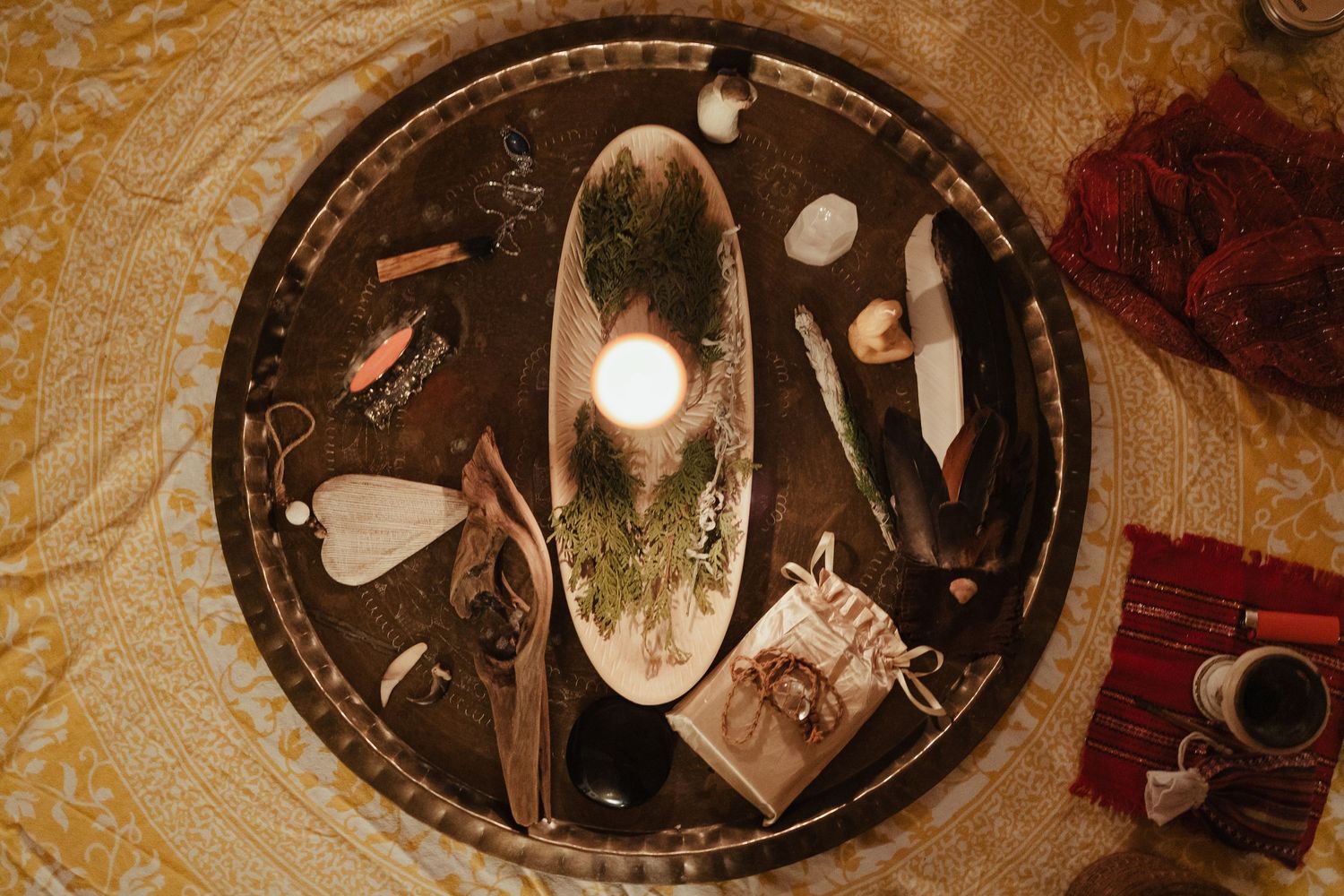 Overhead view of a decorative tray with crystals, candle, feathers, and natural objects arranged as a spiritual altar.