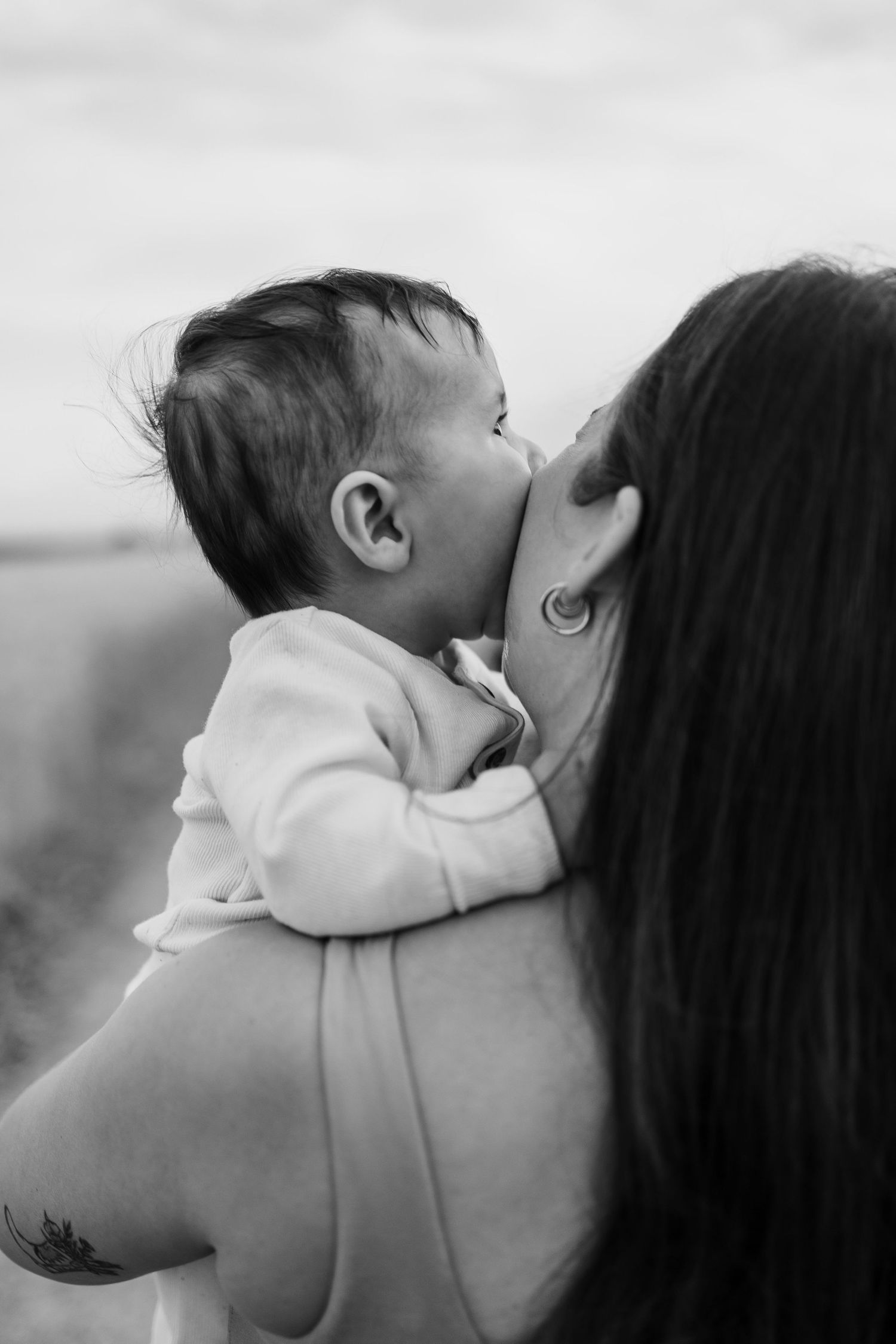Black and white photo of a mother holding her baby outdoors, the infant tenderly nuzzling her cheek.